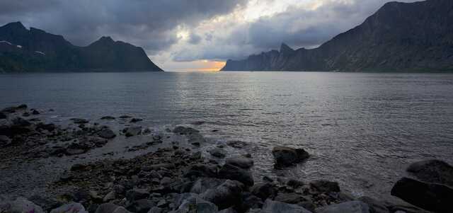 Rocky shoreline with dramatic clouds and distant mountains at sunset