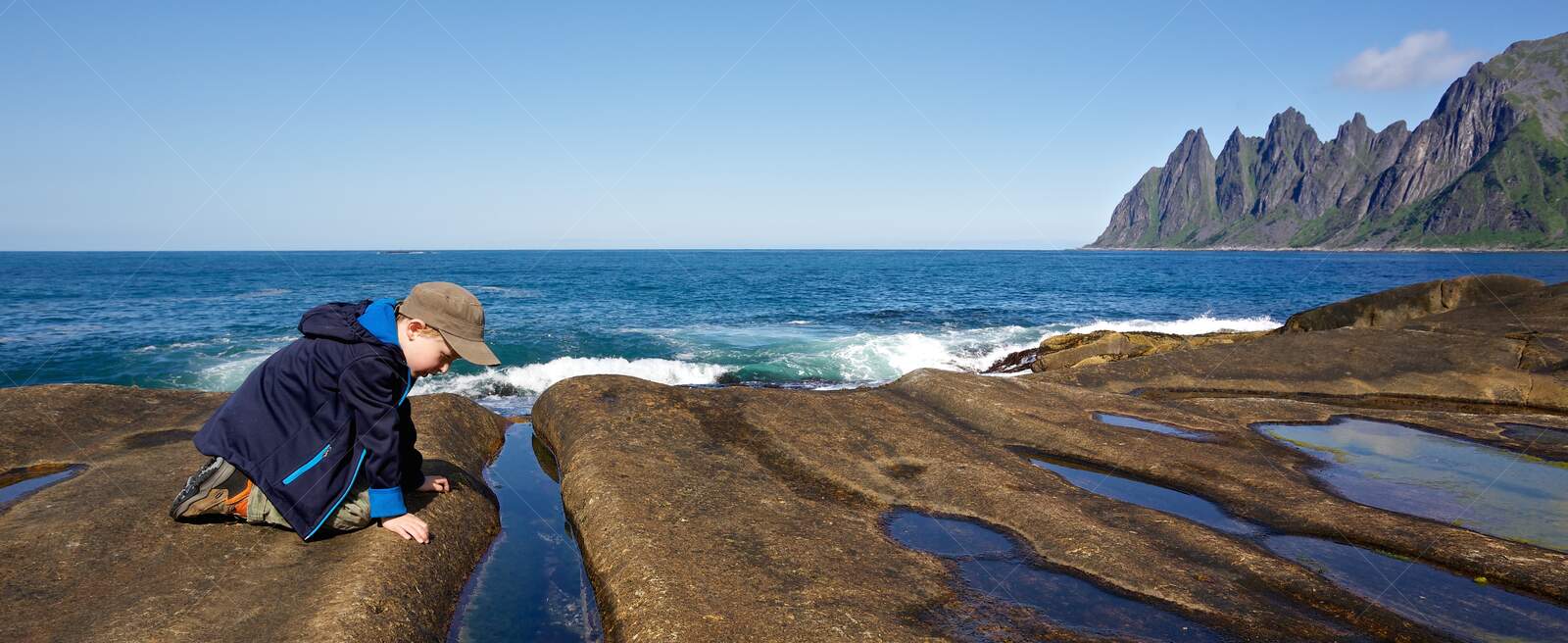 Boy exploring rocky shore with waves and mountains