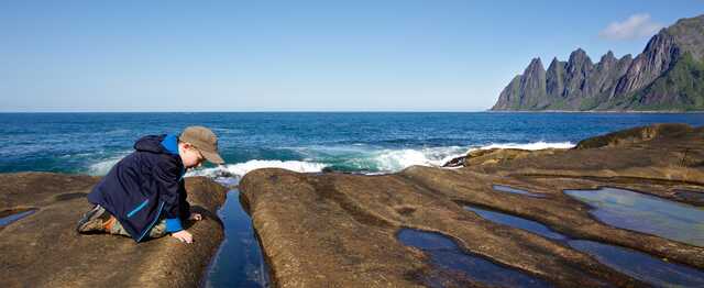Boy exploring rocky shore with waves and mountains