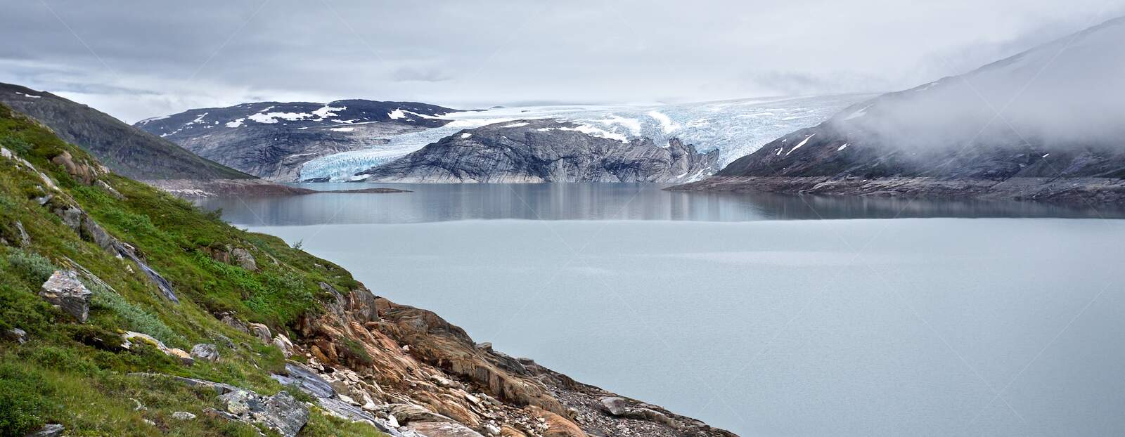 Svartisen glacier and calm lake with rocky shoreline
