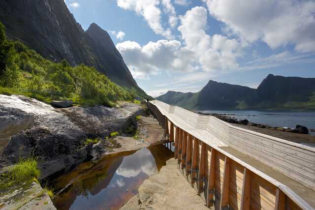 Wooden walkway along rocky coast with mountains in Norway