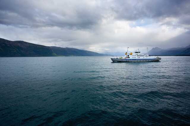 Ferry sailing on a fjord with cloudy sky and mountains