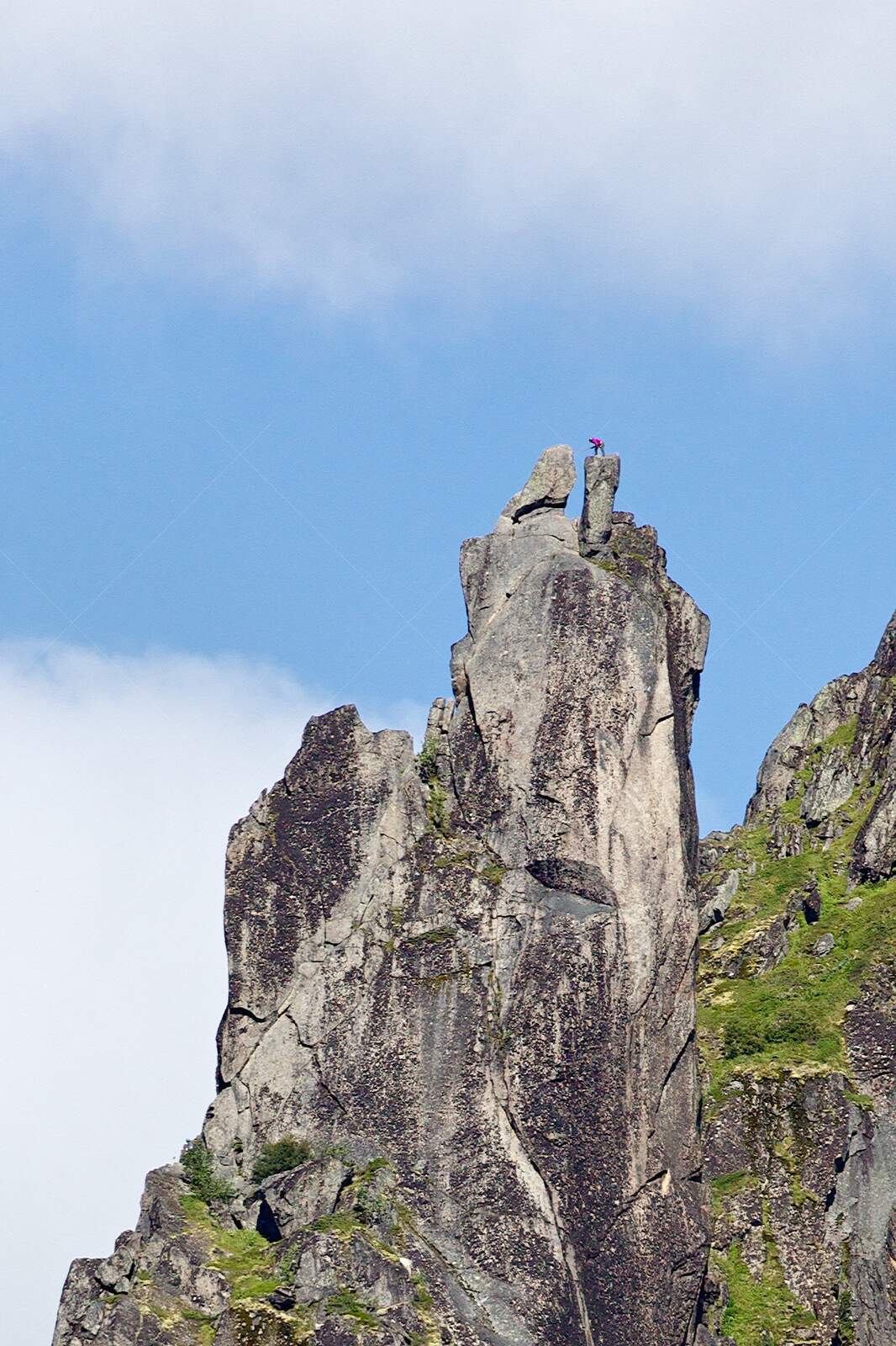 Climber on jagged rocky peak under blue sky