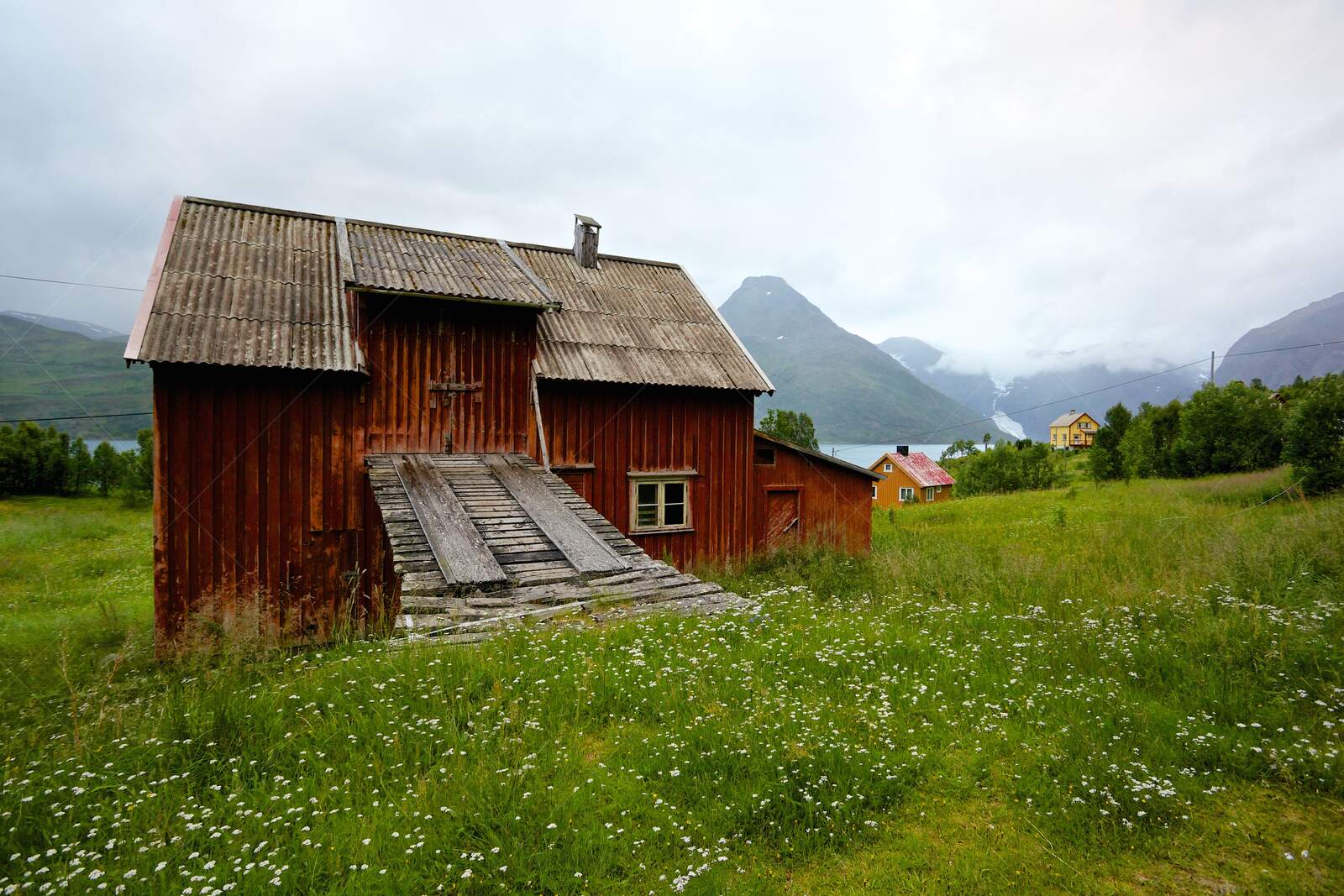 Rustic red wooden barn in a green meadow with mountain backdrop