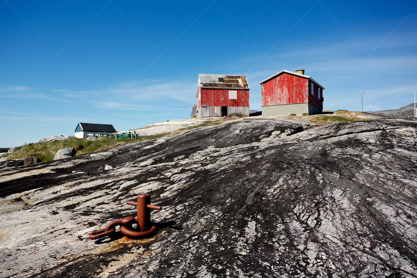 Rustic red houses in Nanortalik, on rocky terrain under clear blue sky