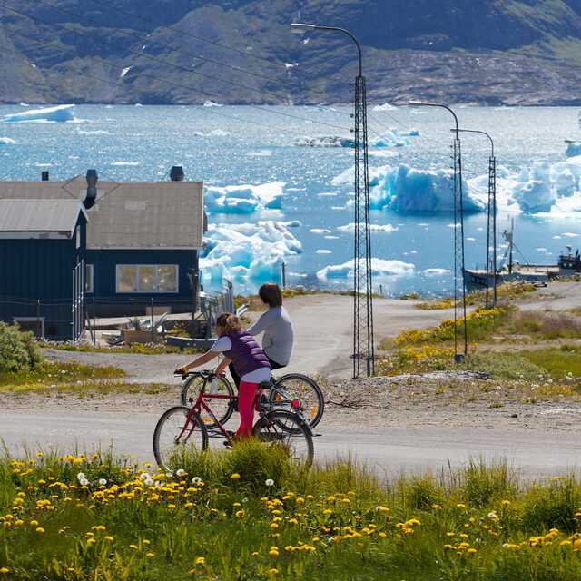 Two people cycling near iceberg-filled fjord in Greenland, Narsaq