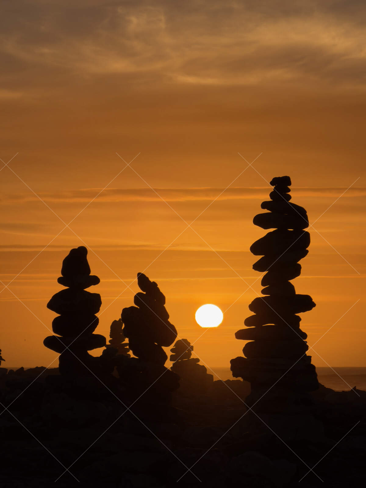 Stacked Stone Cairns at Sunset Silhouetted Against Orange Sky